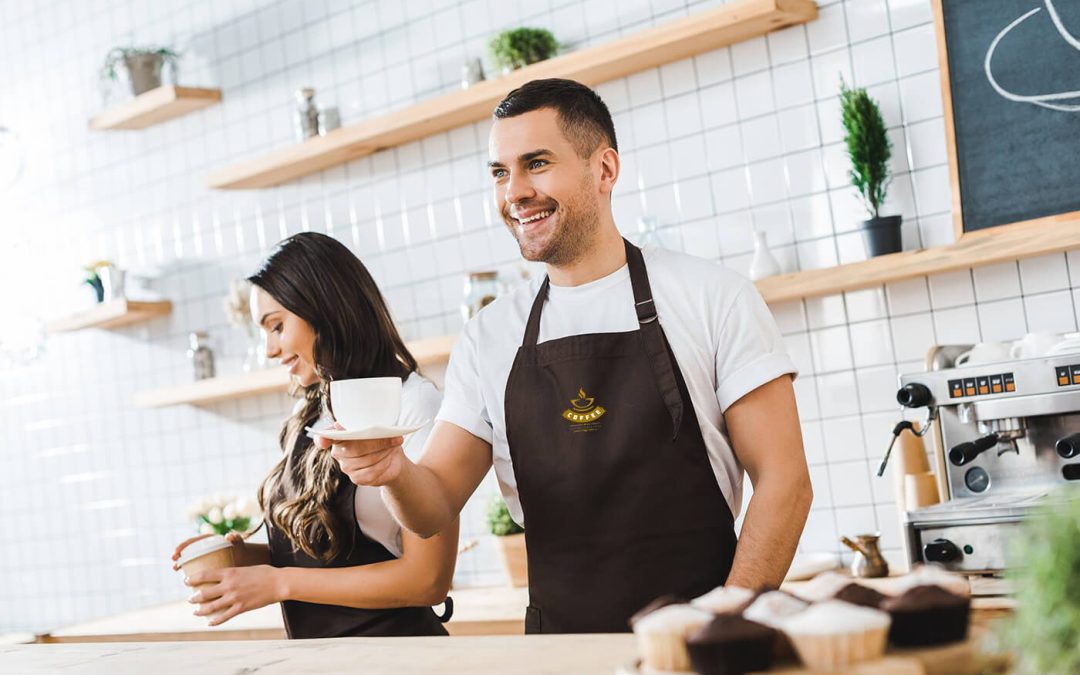 Smiling barista and colleague wearing branded brown aprons while serving coffee